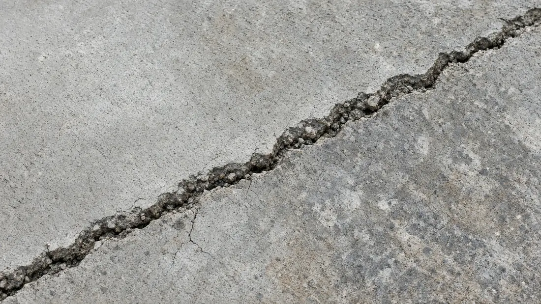 Close-up of a diagonal crack in a gray concrete slab, showing exposed aggregate